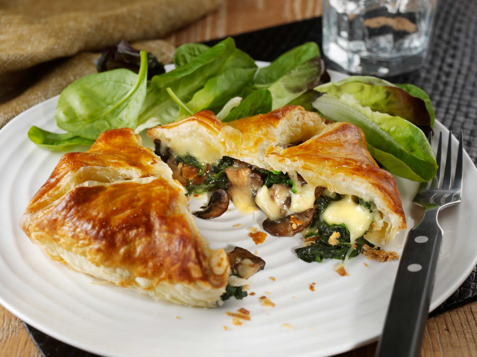 A camembert, spinach & mushroom parcel, cut open, with salad leaves around it.