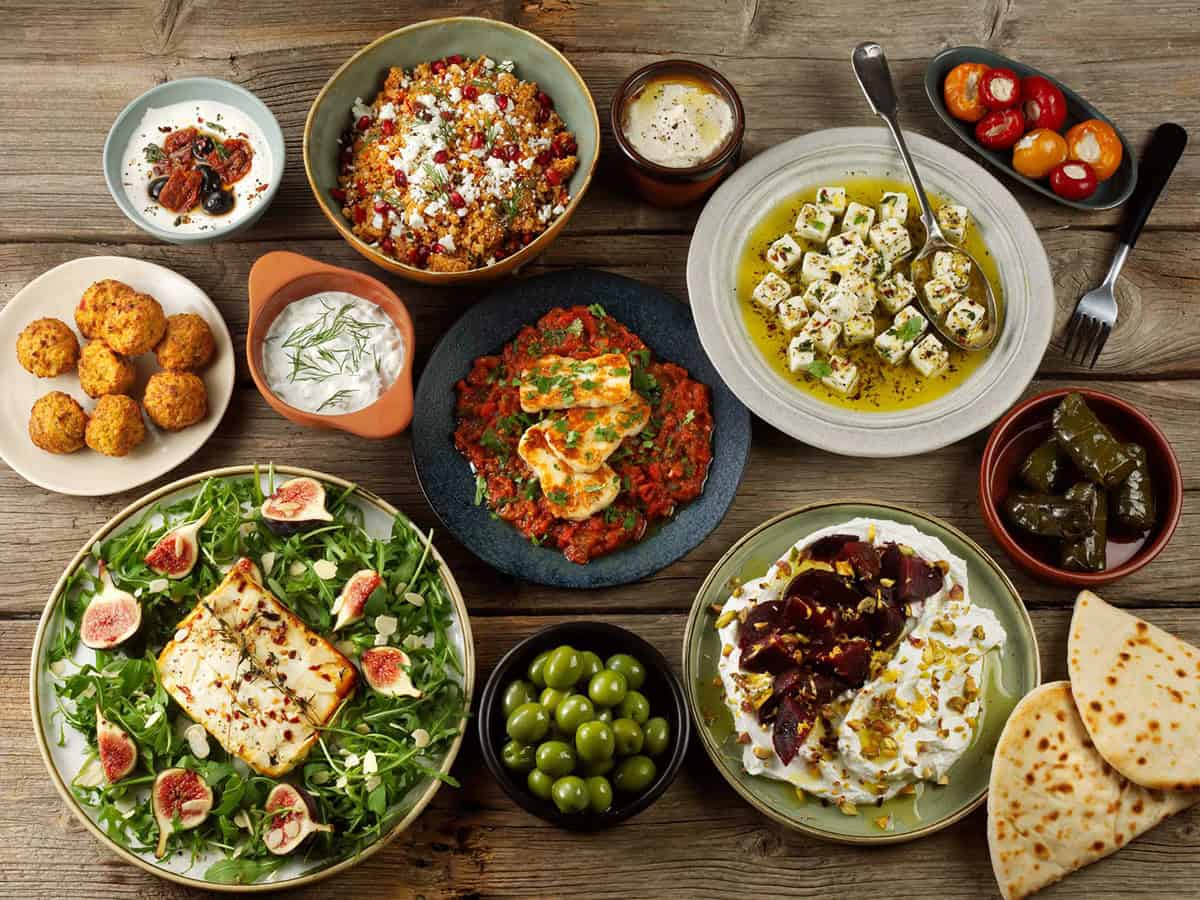 Aerial view of mezze feta, halloumi, labneh and whipped feta presented in different dishes with olives, stuffed chillis and other assorted food plates.